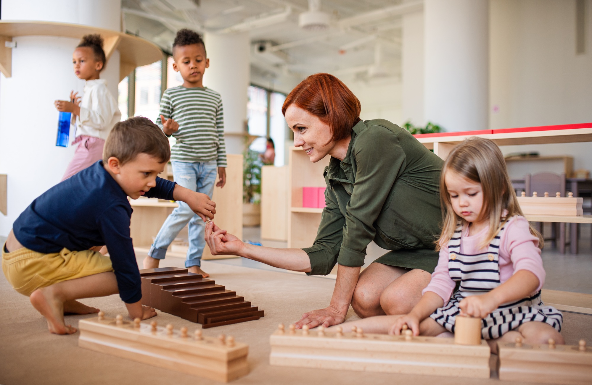 Nursery school children with teacher sitting on floor indoors in classroom, montessori learning.